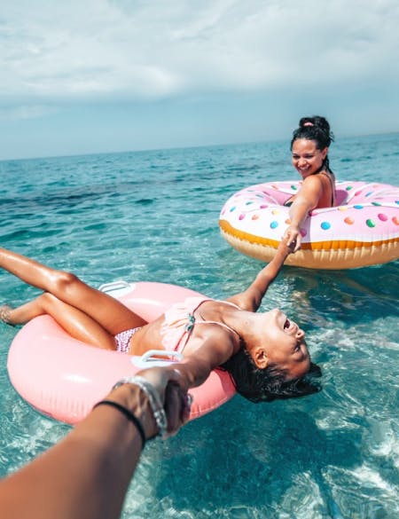 daughter-and-mother-at-the-beach-swimming-with-donut-floats-in-blue-sea